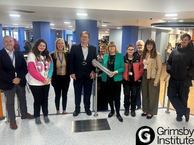 Staff and students holding time capsule in heart of Grimsby Institute campus.